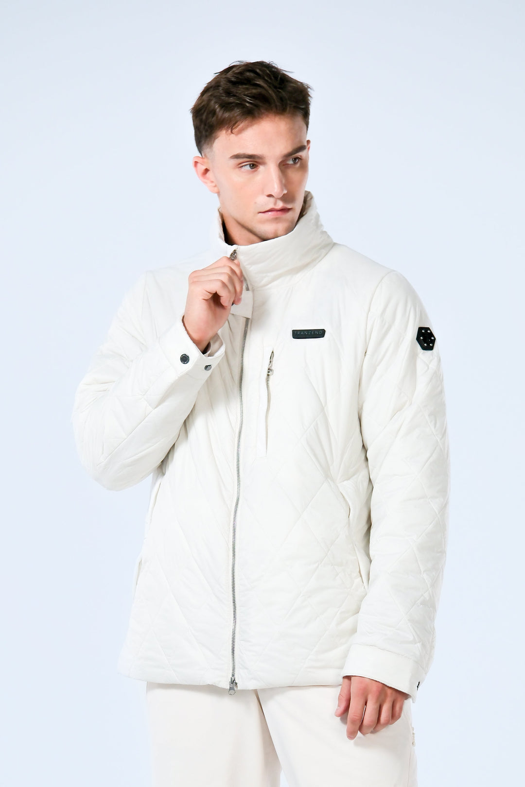 Man wearing a white heated puffer jacket with a white insulated snow trousers on a light gray background